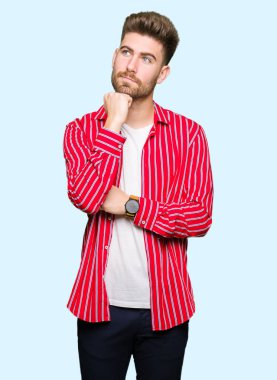 Genç yakışıklı giyen kırmızı gömlek çene düşünme hakkında soru, dalgın ifade üzerine el ile adam. Düşünceli yüzüyle gülümsüyor. Şüphe kavramı.
