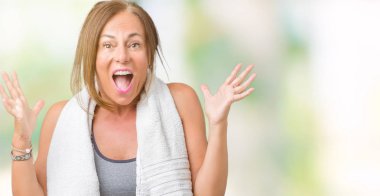 Spor giysi ve bir havlu üzerinde giyen güzel orta yaş kadın deli kutluyor arka plan izole ve başarı için kaldırdı kollarını açarak hayrete ve heyecanlı çığlık gözleri açık. Kazanan kavramı