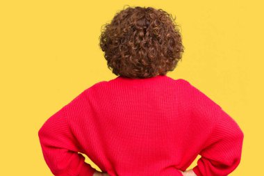 Güzel orta ager üst düzey kadın kırmızı kış kazak izole arka plan ayakta geriye doğru uzakta silah ile vücut üzerinde seyir üzerinde