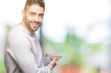 Açık el ile doğal gülümseyen girmek için davet izole arka plan üzerinde sweatshirt giyen genç yakışıklı adam