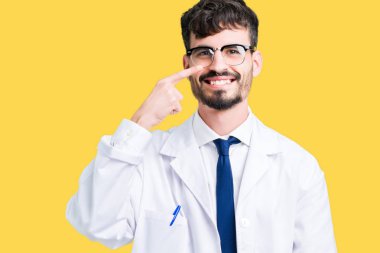 Beyaz önlük üzerinde izole giyen genç profesyonel bilim adam arka plan işaretçi el parmak yüz ve burun, neşeli gülümseyen