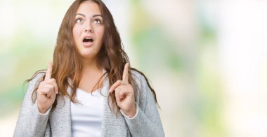 Artı boyutu genç kadın güzel kış ceket izole arka plan üzerinde hayret ve yukarıya bakıyor ve parmakları ile işaret ve silah kaldırdı şaşırttı.