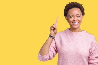 Güzel, genç, Afro-Amerikalı bir kadın izole edilmiş arka planda bir numarayı gösterip işaret ederken kendine güvenen ve mutlu bir şekilde gülümsüyor..