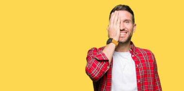 Yüz ve sürpriz duygu kendine güvenen gülümseme ile el ile bir göz kaplayan rahat gömlek giyen yakışıklı adam.