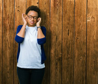 Yüksek sesle müzik gürültü rahatsız ifade parmaklarıyla kulaklarıyla kapsayan izole arka plan üzerinde gözlük takan genç güzel Afrikalı-Amerikalı kadın. Sağır kavramı.