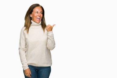 Seyir ve başparmak yanında yukarıyı mutlu yüz ile gülümseyen izole arka plan üzerinde kış kazak giyen güzel orta yaş yetişkin kadın.