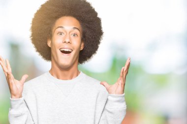 Afrikalı-Amerikalı genç afro saçlı deli ve çığlık kaldırdı ve açık gözleri heyecanlı silah ile başarı için hayran sportif kazak kutluyor giyiyor. Kazanan kavramı