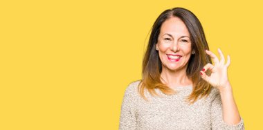 Güzel orta yaş giyen moda kazak el ve parmaklar ok işaretiyle yapıyor olumlu gülümseyen kadın. Başarılı ifade.