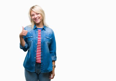 Genç güzel sarışın kadın el ile jest kadar mutlu başparmak yapıyor izole arka planda denim ceket giyiyor. Başarı göstererek kameraya bakarak ifadeyi onaylama.