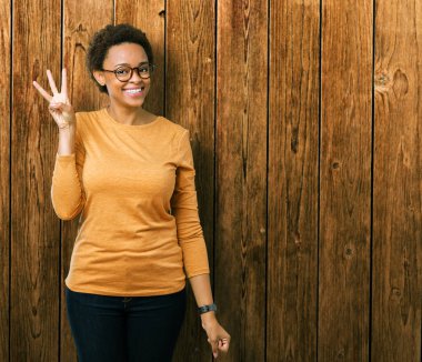 Genç güzel Afrikalı-Amerikalı kadın gözlük gösterilen ve parmakları ile işaret izole arka plan üzerinde ise kendinden emin ve mutlu gülümseyerek üçüncüsü.