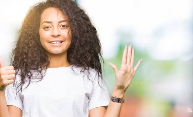 Kıvırcık saçlı gösterilen ve parmakları ile işaret casual beyaz t-shirt giyen genç güzel kız kendinden emin ve mutlu gülümseyerek süre 6 numara.