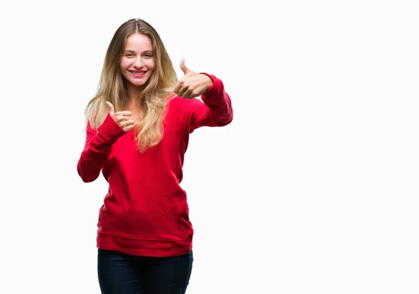 年轻美丽的金发碧眼的女人穿着红色毛衣在孤立的背景 赞同做积极的手势 竖起大拇指微笑 并为成功高兴 看着镜头 赢家的手势 — 图库照片