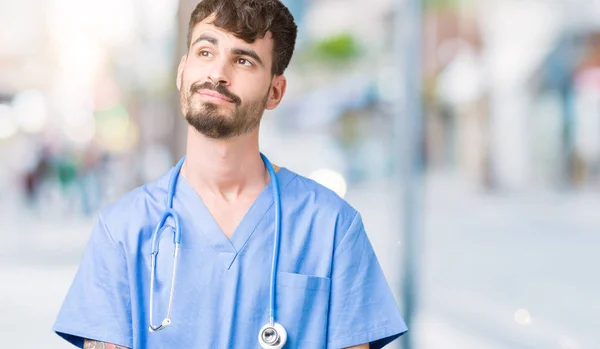 年轻英俊的护士男子穿着外科医生制服在孤立的背景微笑看着一边 盯着思考 — 图库照片
