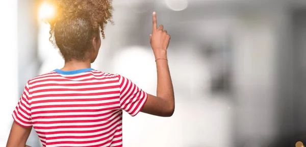 Beautiful young african american woman over isolated background Posing backwards pointing behind with finger hand