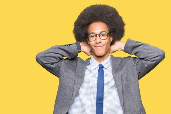 Young african american business man with afro hair wearing glasses Relaxing and stretching with arms and hands behind head and neck, smiling happy