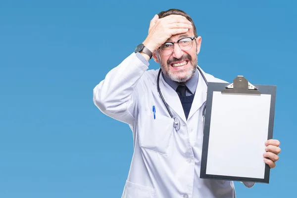 Middle age senior hoary doctor man holding clipboard isolated background stressed with hand on head, shocked with shame and surprise face, angry and frustrated. Fear and upset for mistake.