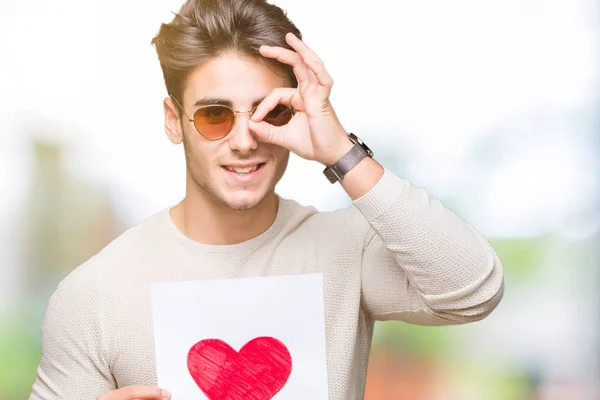 Joven Hombre Guapo Sosteniendo Tarjeta Con Corazón Rojo Sobre Fondo — Foto de Stock