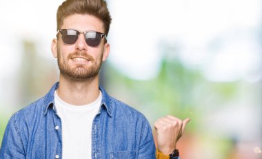 Seyir ve başparmak yanında yukarıyı mutlu yüz ile gülümseyen denim ceket giyen genç yakışıklı zarif adam.