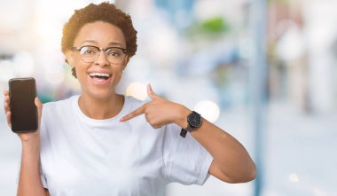 Genç Afro-Amerikan kadın gösteren smartphone ekran kendisi için sürpriz yüz işaret parmağı ile izole arka plan üzerinde