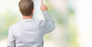 Bir kazak izole üzerinde giyen yakışıklı orta yaş üst düzey adam arka plan geriye doğru arkasında parmak eliyle işaret Posing