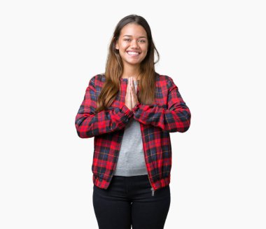 Birlikte emin gülümseyen bağışlanmak ellerle dua izole arka plan üzerinde bir ceket giyen genç güzel esmer kadın.