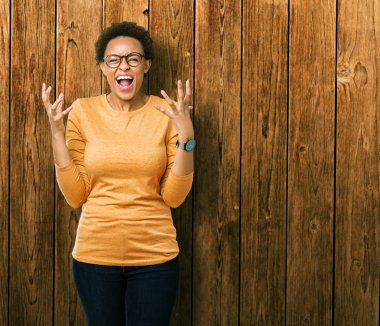 Genç güzel Afrikalı-Amerikalı kadın üzerinde gözlük takan arka plan deli izole ve deli bağırarak ve agresif ifade ve silah kaldırdı bağırıyor. Hayal kırıklığı kavramı.