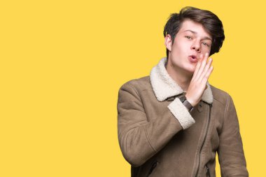 Genç yakışıklı adam giyen kış ceket izole arka plan üzerinde el gizli söylenti, kötü niyetli konuşma konuşma fısıldayarak söylemek dudaklarından