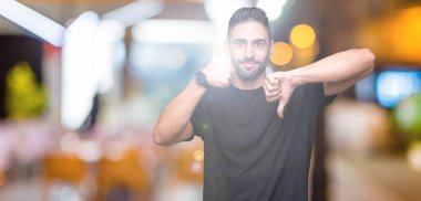 Yakışıklı delikanlı izole arka plan yapmaya başparmak yukarı ve aşağı, anlaşmazlık ve anlaşma ifade üzerinde. Deli çatışma