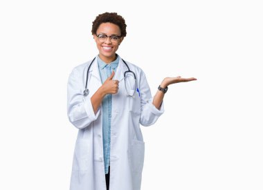 Üzerinde tıbbi ceket giyen genç Afro-Amerikan doktor kadın arka plan gösteren palm el ve iş tamam jestle başparmak yukarıya, mutlu ve neşeli gülümseyen izole