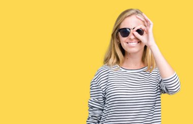 Güzel genç kadın gülümsüyor, parmakları ile mutlu yüz üzerinden seyir göz el ile ok jest yapıyor izole arka plan üzerinde güneş gözlüğü takıyor.