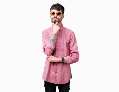 Genç yakışıklı adam çene düşünme hakkında soru, dalgın ifade üzerine el ile izole arka plan üzerinde güneş gözlüğü takıyor. Düşünceli yüzüyle gülümsüyor. Şüphe kavramı.