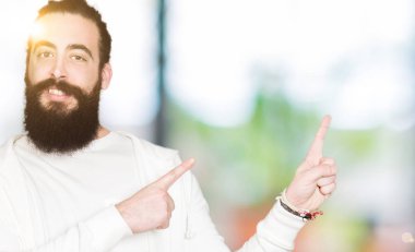 Uzun saç ve sakal gülümseyen ve iki elleri ve parmakları ile tarafına işaret kamera bakarak sportif sweatshirt giyen genç adamla.