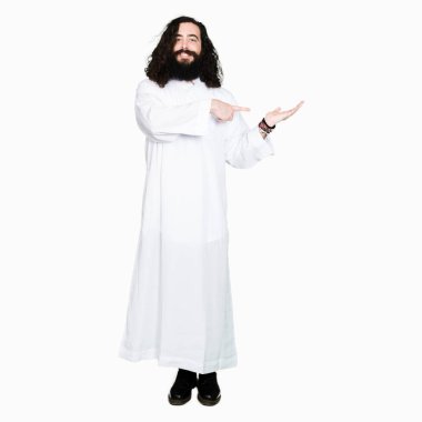 Hayret ve el ile sunulması ve parmak ile işaret ederken kameraya gülümseyen İsa Mesih giyinen adam.