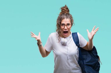 Sırt çantası ve kulaklık üzerinde giyen genç esmer öğrenci kız deli kutluyor arka plan izole ve başarı için kaldırdı kollarını açarak hayrete ve heyecanlı çığlık gözleri açık. Kazanan kavramı