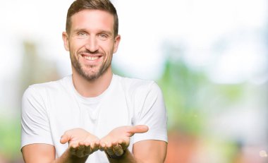 Casual beyaz t-shirt gülen birlikte alma veya jest veren el avuç içi ile giyen yakışıklı adam. Ayrı tutma ve koruma