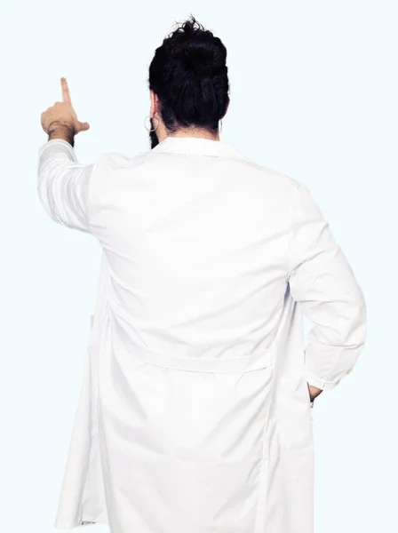 聴診器と医療のコートを身に着けている長い髪の医者指手の背後後方を指すポーズ — ストック写真