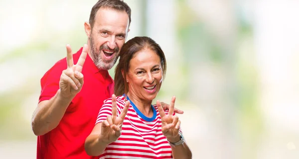 中年勝利のサインをやって指を表示するカメラを笑みを浮かべて隔離された背景に愛のヒスパニックのカップル — ストック写真