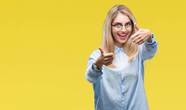 Young beautiful blonde business woman wearing glasses over isolated background approving doing positive gesture with hand, thumbs up smiling and happy for success. Looking at the camera, winner gesture.