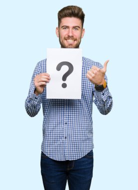 Yakışıklı delikanlı ok işareti, başparmak ile parmak, mükemmel işareti yapıyor kocaman bir gülümseme ile kağıt soru işareti ile mutlu holding