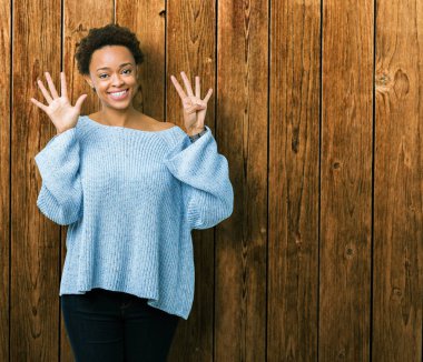 Genç güzel Afrikalı Amerikalı kadın izole arka planda gösteren bir kazak giyiyor ve parmak numarası dokuz ile işaret kadar emin ve mutlu gülümseyen.