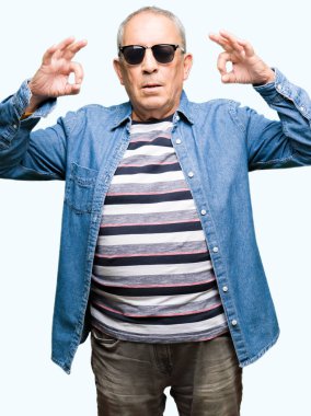 Yakışıklı komuta sizde giyen denim ceket ve güneş gözlüğü dinlenmek ve gülümseyen gözlerle kapalı parmak jestle meditasyon yapıyor. Yoga kavramı.