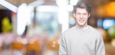 Yüz üzerinde mutlu ve serin bir gülümseme ile izole arka plan üzerinde sweatshirt giyen genç yakışıklı sportif adam. Şanslı kişi.