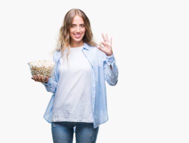 Parmak, mükemmel sembolü ile ok işareti yapıyor izole arka plan üzerinde patlamış mısır yemek güzel sarışın genç kadın