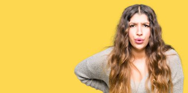 Genç güzel kadın giyiyor Kış Giysi acı dokunmadan el ile geri, kas ağrısı, sırt ağrısı,