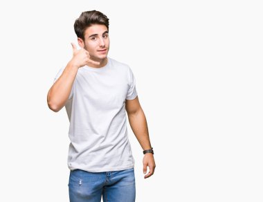 Genç yakışıklı yapıyor gülümseyen izole arka plan üzerinde beyaz t-shirt giyen adam telefon hareketi ile el ve parmak telefonda konuşuyor gibi. Kavramları iletişim.