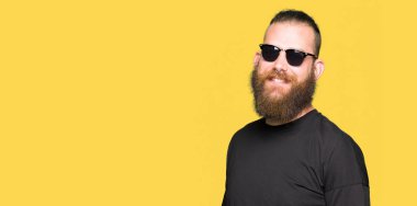 Genç hipster adam yüzünde mutlu ve güzel bir gülümseme ile güneş gözlüğü takıyor. Şanslı kişi.