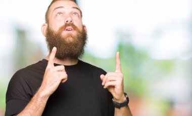 Rahat t-shirt giyen genç sarışın adam hayret ve yukarıya bakıyor ve parmakları ile işaret ve silah kaldırdı şaşırttı.