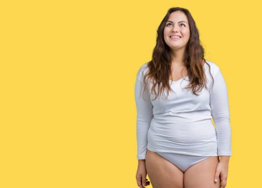 Artı boyutu genç overwight kadın güzel üzerinde beyaz iç çamaşırı giyiyor arka plan görünümlü yan ve dik dik bakma uzağa düşünce gülümseyen izole.