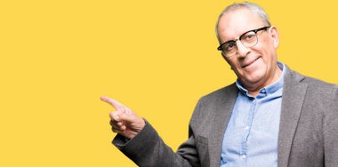 Yüzünde, kocaman bir gülümseme ile gözlük takan yakışıklı üst düzey businesss adam kameraya bakarak yan el ve parmak ile işaret.