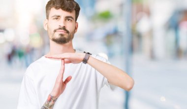 İzole arka plan yapıyor zaman aşımı jest elle, sinirli ve ciddi bir yüz üzerinde beyaz t-shirt giyen genç yakışıklı adam